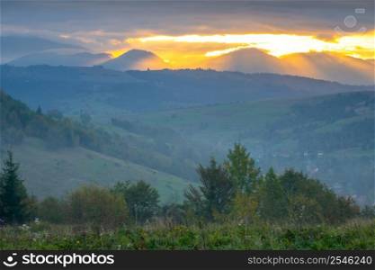 Summer evening in the Ukrainian Carpathians. Wooded mountains and small villages. The last rays of the sun break through the dramatic clouds. Dramatic Sunset Over the Ukrainian Carpathians