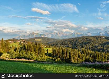 Summer evening mountain village outskirts with houses on hill top and Tatra range behind (Poland)