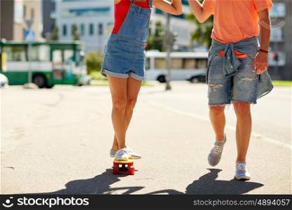 summer, extreme sport and people concept - happy teenage couple riding short modern cruiser skateboard on city street