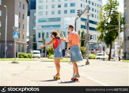 summer, extreme sport and people concept - teenage couple riding short modern cruiser skateboards on city street