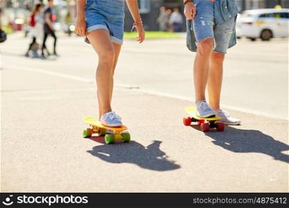 summer, extreme sport and people concept - teenage couple riding short modern cruiser skateboards on city street