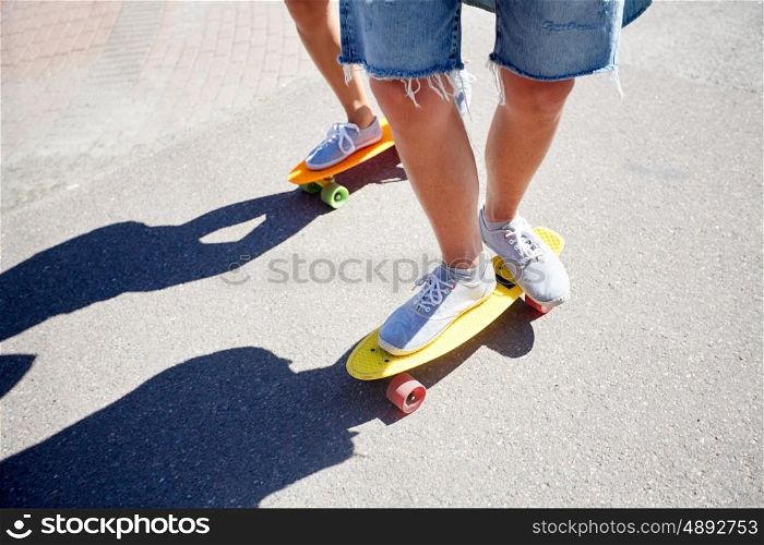 summer, extreme sport and people concept - teenage couple riding short modern cruiser skateboards on city road