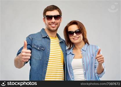 summer, eyewear and people concept - happy couple in sunglasses showing thumbs up over grey background. happy couple in sunglasses showing thumbs up