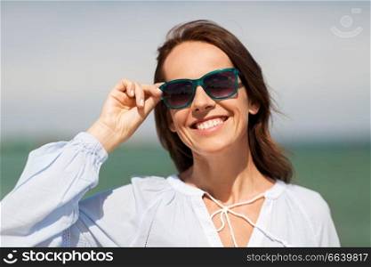 summer, eyewear and people concept - happy smiling woman in sunglasses on beach. happy smiling woman in sunglasses on summer beach