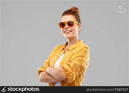 summer, eyewear and people concept - smiling red haired teenage girl in sunglasses and yellow checkered shirt with crossed arms over grey background. smiling red haired teenage girl in sunglasses