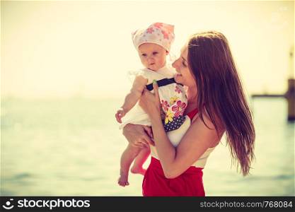 Summer family recreation concept. Mother holding and playing with little baby on beach during summertime.. Mother playing with baby on beach