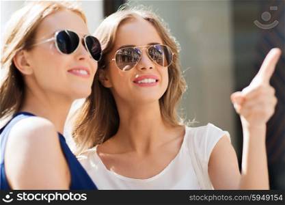 summer, fashion, accessories and people concept - happy women in sunglasses pointing finger in city