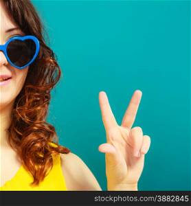 Summer fashion eyes protection concept. Closeup girl long curly hair in blue heart shaped sunglasses making victory hand sign gesture