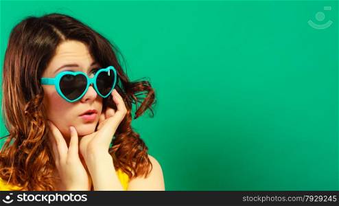 Summer fashion eyes protection concept. Closeup girl long curly hair in heart shaped sunglasses on green vivid color background