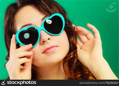 Summer fashion eyes protection concept. Closeup girl long curly hair in heart shaped sunglasses on green vivid color background