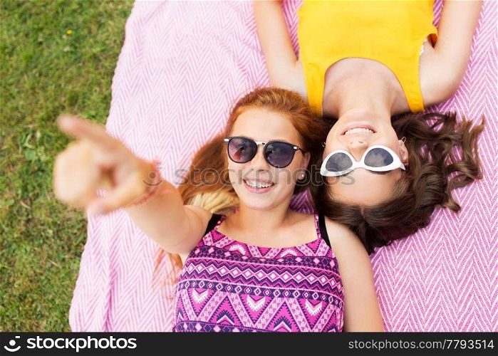 summer fashion, eyewear and leisure concept - smiling teenage girls in sunglasses lying on picnic blanket. teenage girls in sunglasses on picnic blanket