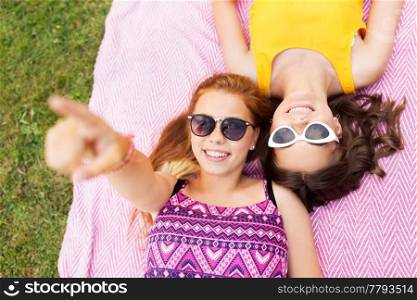 summer fashion, eyewear and leisure concept - smiling teenage girls in sunglasses lying on picnic blanket. teenage girls in sunglasses on picnic blanket