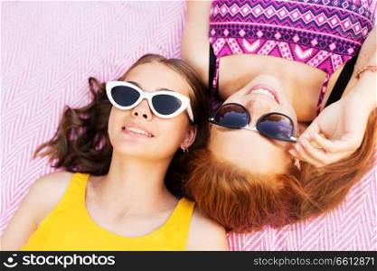 summer fashion, eyewear and people concept - smiling teenage girls in sunglasses lying on picnic blanket. teenage girls in sunglasses on picnic blanket
