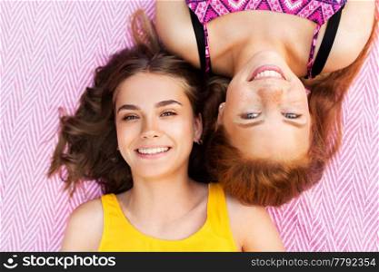 summer fashion, leisure and people concept - smiling teenage girls or friends lying on picnic blanket. smiling teenage girls lying on picnic blanket