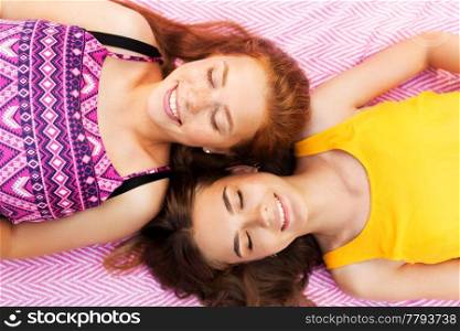 summer fashion, leisure and people concept - smiling teenage girls or friends lying on picnic blanket. smiling teenage girls lying on picnic blanket