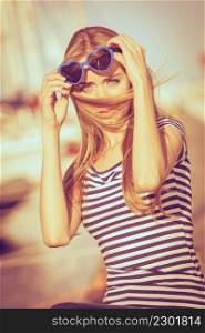 Summer fashion. Portrait girl in blue heart shaped sunglasses enjoying summer breeze at sunset in marina
