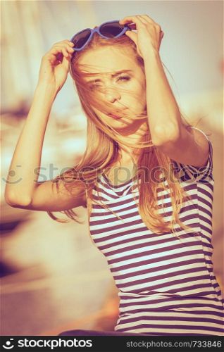 Summer fashion. Portrait girl in blue heart shaped sunglasses enjoying summer breeze at sunset in marina