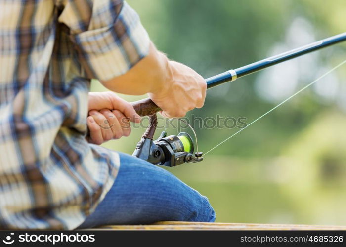 Summer fishing. Close up of guy sitting on bridge and fishing