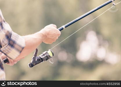 Summer fishing. Young guy in hat sitting on bridge and fishing