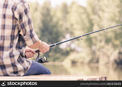 Summer fishing. Young guy in hat sitting on bridge and fishing