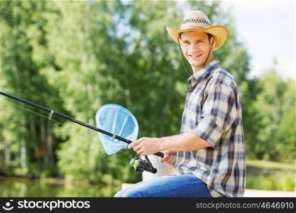 Summer fishing. Young guy in hat sitting on bridge and fishing