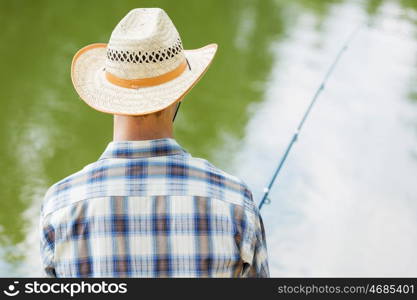 Summer fishing. Young guy in hat sitting on bridge and fishing