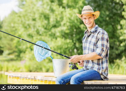 Summer fishing. Young guy in hat sitting on bridge and fishing