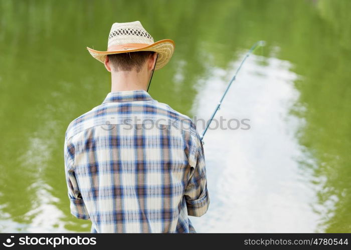 Summer fishing. Young guy in hat sitting on bridge and fishing