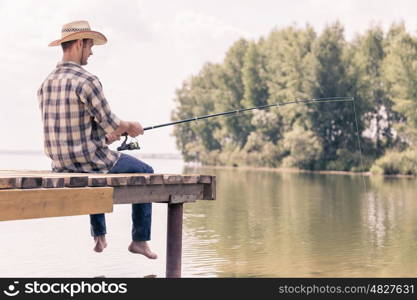 Summer fishing. Young guy in hat sitting on bridge and fishing