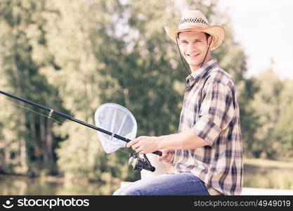 Summer fishing. Young guy in hat sitting on bridge and fishing