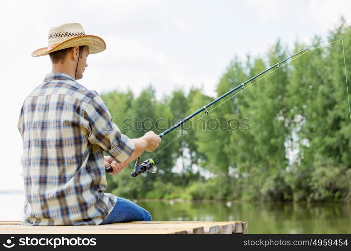 Summer fishing. Young guy in hat sitting on bridge and fishing