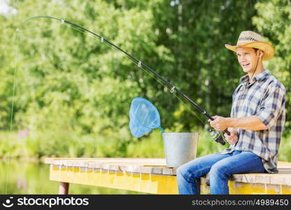 Summer fishing. Young guy in hat sitting on bridge and fishing