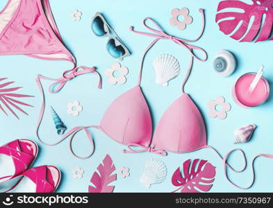 Summer flat lay. Pink woman’s beach accessories  swimsuit bikini , sandals, drink, sunglasses , sea shells and tropical leaves on blue background, top view. Summer holiday concept. Tropical vacation