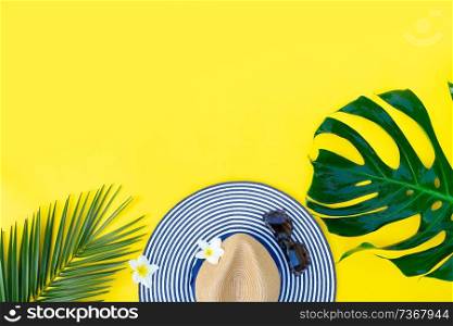 Summer flat lay scenery with hat and green leaves on bright yellow background, top view border with copy space. Summer flat lay scenery
