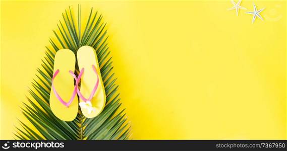 Summer flat lay top view scenery on yellow background with palm leaf and flip flops, banner with copy space. Summer flat lay scenery