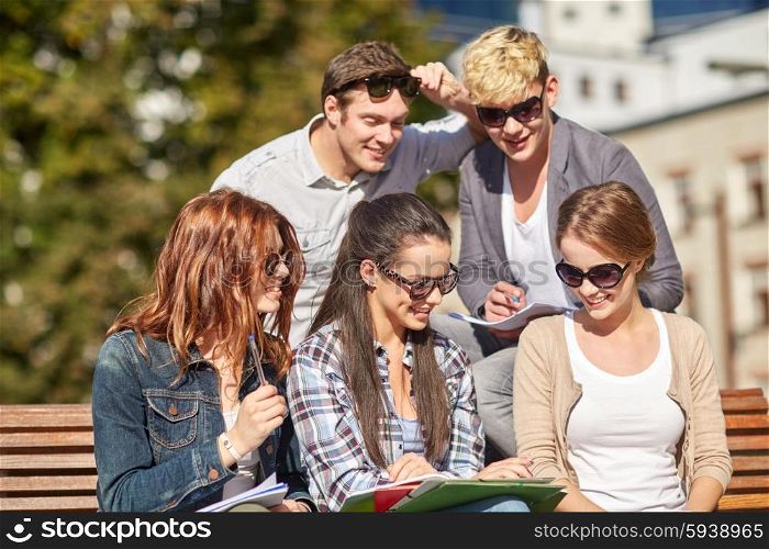 summer, friendship, education and teenage concept - group of happy students with notebooks learning at campus