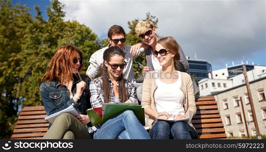 summer, friendship, education and teenage concept - group of happy students with notebooks learning at campus