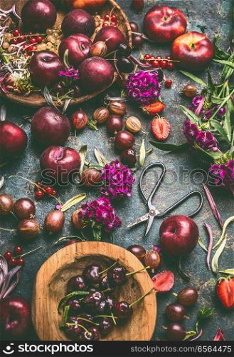 Summer fruits and berries still life on dark rustic background with wooden bowls and garden flowers, top view