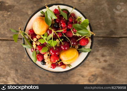 Summer fruits in enamelled metal bowl on wooden table