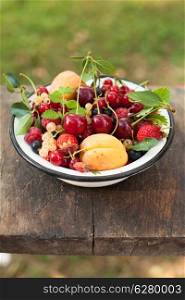 Summer fruits in enamelled metal bowl on wooden table