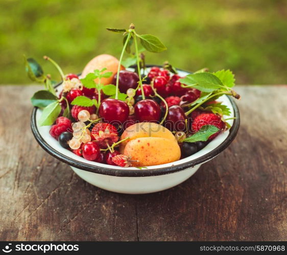 Summer fruits in enamelled metal bowl on wooden table. Summer fruits