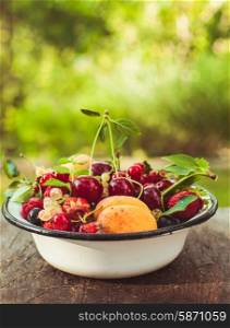 Summer fruits in enamelled metal bowl on wooden table. Summer fruits