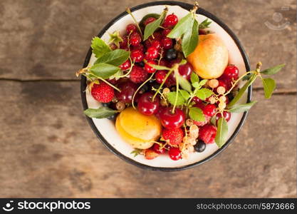 Summer fruits in enamelled metal bowl on wooden table. Summer fruits