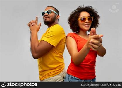 summer, fun and people concept - happy smiling african american couple in sunglasses making finger gun gesture over grey background. african couple in sunglasses makes finger gun