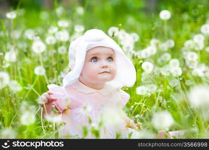 Summer fun, sweet little girl, sitting and blowing dandelion on the meadow
