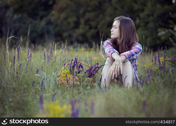 summer. Girl teenager sitting alone in a meadow. Near the basket with sage