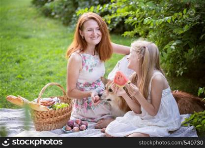 Summer - happy family at a picnic. Cheerful mom, daughter and basket with meal on the green grass