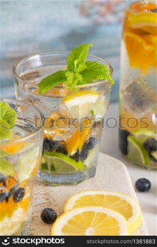 Summer healthy cocktails of citrus infused waters, lemonades or mojitos, with lime lemon orange blueberries and mint, diet detox beverages, in glasses on light background