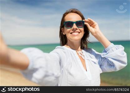summer holidays and leisure concept - happy smiling woman in sunglasses taking selfie on beach. woman in sunglasses taking selfie on summer beach
