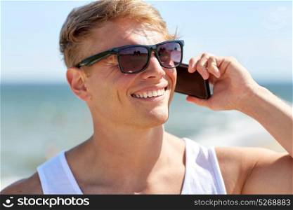 summer holidays and people concept - close up of happy smiling young man in sunglasses calling on smartphone on beach. smiling man calling on smartphone on summer beach
